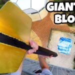 Drone‑shot thumbnail of a person on a tall tower, gripping a large gold tool toward a blue ice block on the ground far below; bold caption reads 'GIANT ICE BLOCK!' indicating a stunt video.