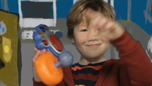 Smiling young boy plays with a colorful toy controller indoors, waving hello.