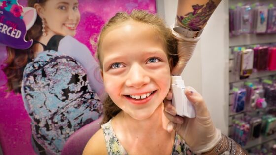 Smiling young girl in a store as a gloved professional uses a white device on her cheek, with colorful product displays in the background.