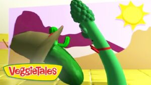 Animated VeggieTales scene: a green cucumber and broccoli arm-wrestle/high-five on a sunny stage, with VeggieTales logo bottom-left.