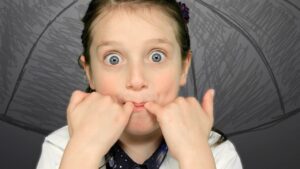 Young girl with wide blue eyes making a silly face, pulling the corners of her mouth with her fists.