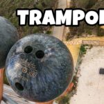 High-angle thumbnail of two bowling balls on a railing, looking down at a fenced yard with a square trampoline pad and a bold 'TRAMPOLINE' caption.