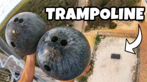 High-angle thumbnail of two bowling balls on a railing, looking down at a fenced yard with a square trampoline pad and a bold 'TRAMPOLINE' caption.