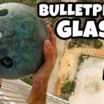 Thumbnail: person on a balcony pressing a bowling ball against a glass panel, implying a bulletproof glass test, with bold 'BULLETPROOF GLASS' text in the corner.