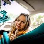 Young girl in a car looking worried, with the dashboard and two drink cups visible nearby.