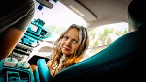 Young girl in a car looking worried, with the dashboard and two drink cups visible nearby.