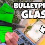 Thumbnail of a person striking bright green bulletproof glass on a high balcony, with bold 'BULLETPROOF GLASS' text overlay and a white arrow.