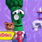 Green veggie character in a suit with a red striped tie stands beside a teddy bear in a purple room, VeggieTales branding visible in the corner.
