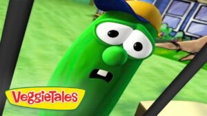 Green VeggieTales cucumber character with a cap, looking surprised in a bright park scene with the VeggieTales logo in the corner