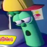 Green cucumber character from VeggieTales wearing a yellow construction helmet, leaning on a white surface with the VeggieTales logo visible in the corner.