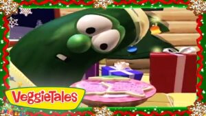 Larry the Cucumber from VeggieTales leans toward a pink birthday cake with presents nearby, inside a festive holiday border with the VeggieTales logo.