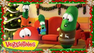 VeggieTales characters—tomato, cucumber in a brown Christmas sweater, and broccoli—sitting in a festively decorated living room with a Christmas tree.