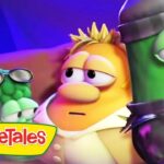 VeggieTales scene with cartoon vegetable characters on a colorful stage and the VeggieTales logo in the bottom-left corner.