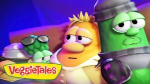VeggieTales scene with cartoon vegetable characters on a colorful stage and the VeggieTales logo in the bottom-left corner.