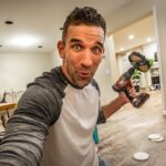 Man selfie holding a cordless drill indoors, mid-project in a bright kitchen/garage space, surprised expression.