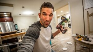 Man selfie holding a cordless drill indoors, mid-project in a bright kitchen/garage space, surprised expression.