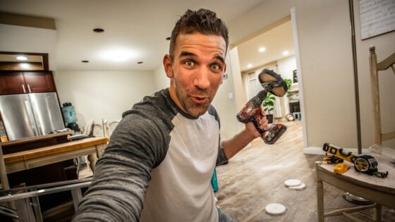 Man selfie holding a cordless drill indoors, mid-project in a bright kitchen/garage space, surprised expression.