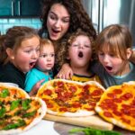 A mother and four children hover over three pepperoni and veggie pizzas on a kitchen counter, mouths agape in excitement.