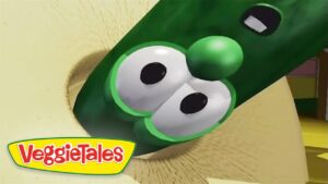 Close-up of a green cucumber cartoon head with big eyes from VeggieTales, with the VeggieTales logo in the corner.