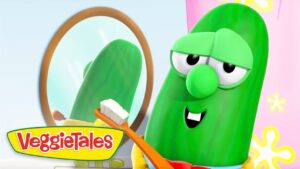Green VeggieTales cucumber brushing its teeth with an orange toothbrush, mirror reflected behind.