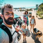 Man with a backpack taking a selfie as his family and their dog walk toward the beach beside a parked SUV.