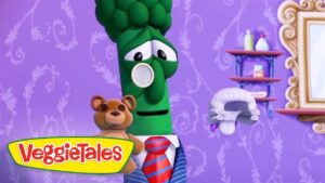 VeggieTales scene: a green broccoli character in a suit with a teddy bear on a purple patterned background, logo bottom left.