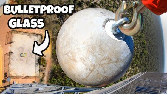 Drone view of a large round ballast sphere attached to a crane on a high-rise balcony, with 'BULLETPROOF GLASS' text overlay