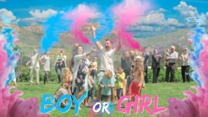 Outdoor gender reveal celebration with a crowd cheering as blue and pink powder bursts, and the bold 'BOY OR GIRL' text at the bottom.