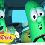 Two green VeggieTales characters riding in a car, smiling at the camera, with the VeggieTales logo in the lower-left corner.