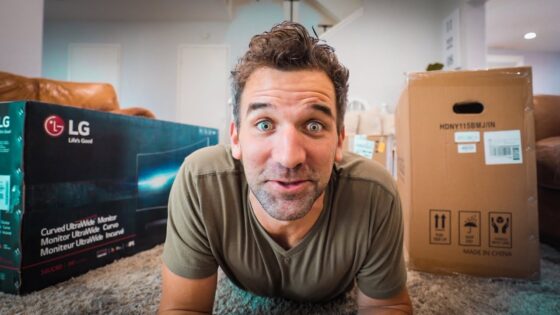 Man lying on a carpeted floor between boxed items, looking up with a surprised expression toward the camera (moving day). My left: an LG TV box; right: a large cardboard box.