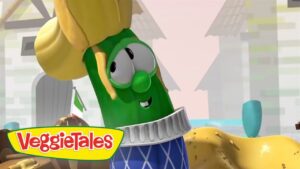 Larry the cucumber from VeggieTales wearing a blue patterned sweater and a yellow hat, smiling at the camera.