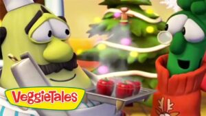 Two VeggieTales characters, a yellow-green chef and a green veggie, lean toward a tray of red apples in a cozy kitchen with a Christmas tree in the background, VeggieTales logo visible.
