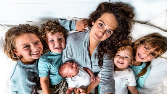 Mother and five children cuddled together on a bed, all smiling at the camera with a newborn infant held by the mother.