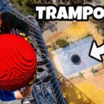Two people on a tall metal scaffold holding a large bright red spiked ball, with an aerial view of a platform with a hole below.
