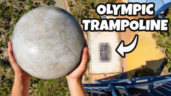 Aerial view of a person holding a large gray sphere above a trampoline setup on a tall structure, with a bold 'OLYMPIC TRAMPOLINE' caption.