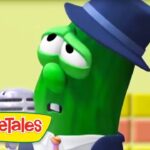 Larry the cucumber from VeggieTales in a blue hat, microphone in hand, on a colorful stage.