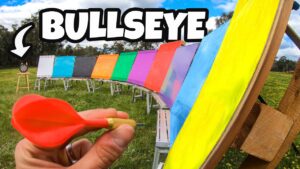 Hand holding a red dart ready to throw at a rainbow-colored target row outdoors, with 'BULLSEYE' text overlaid on the image.