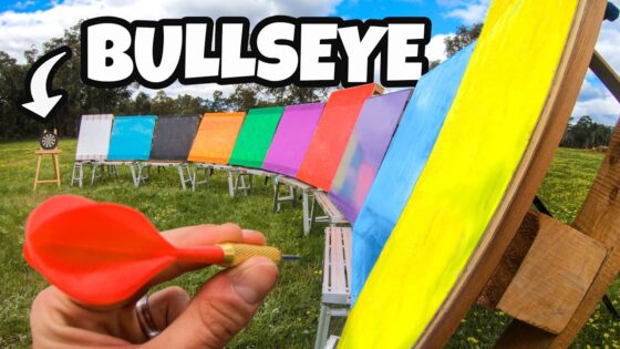 Hand holding a red dart ready to throw at a rainbow-colored target row outdoors, with 'BULLSEYE' text overlaid on the image.