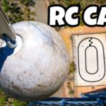 From above: a crane hook grips a weathered gray ball near a small RC car race track, with a bold 'RC CARS' overlay.