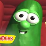 Smiling green cucumber character from VeggieTales with big eyes, inside a colorful set.