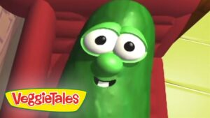Smiling green cucumber character from VeggieTales with big eyes, inside a colorful set.