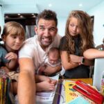 Father with five children around a cluttered table full of coloring supplies, smiling for a selfie.