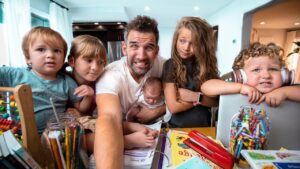 Father with five children around a cluttered table full of coloring supplies, smiling for a selfie.