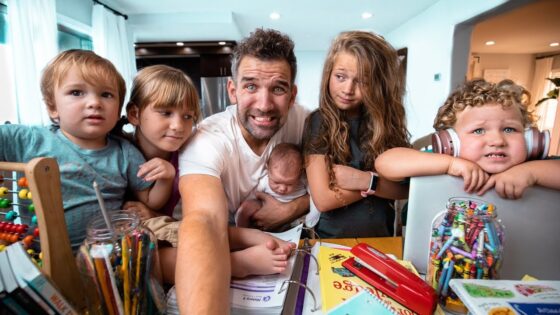 Father with five children around a cluttered table full of coloring supplies, smiling for a selfie.