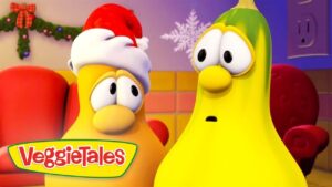 Two VeggieTales characters, one wearing a Santa hat, look surprised in a festive room with holiday decorations and the VeggieTales logo in the corner.