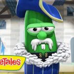 Green VeggieTales cucumber in a blue pirate outfit with a white fur collar, standing in a castle set with the VeggieTales logo.