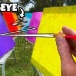 Man throws a small dart at bright colored boards set on stands outdoors, aiming for a bullseye in a field.