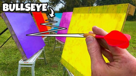 Man throws a small dart at bright colored boards set on stands outdoors, aiming for a bullseye in a field.