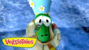 Green cucumber character from VeggieTales wearing a blue hat with daisies and a monocle against a blue background.