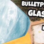 Large, pale-blue glass block suspended by red ropes, viewed from above, with bold 'BULLETPROOF GLASS' text in the corner.